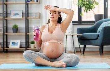 sport and people concept - tired pregnant woman drinking water after yoga at home. pregnant woman drinking water after yoga at home