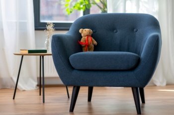 interior, furniture and object concept - modern blue armchair with legs, teddy bear toy and book on table table at home. modern armchair with teddy bear toy at home