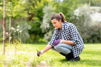 gardening and people concept - happy smiling woman weeding flowerbed at summer garden. woman weeding flowerbed at summer garden