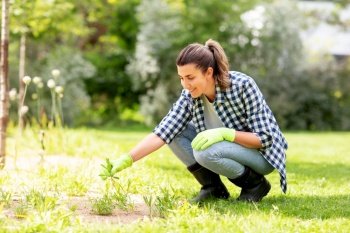 gardening and people concept - happy smiling woman weeding flowerbed at summer garden. woman weeding flowerbed at summer garden