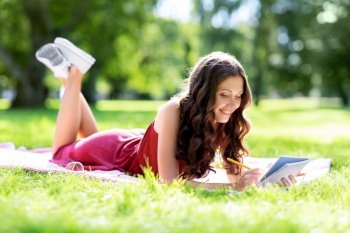 leisure, inspiration and people concept - happy smiling woman writing to diary or notebook lying on picnic blanket at summer park. happy woman with diary or notebook at park