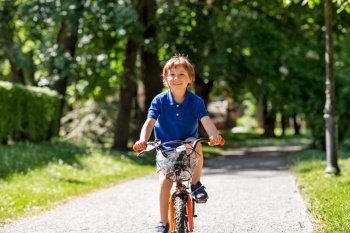 childhood, leisure and people - happy smiling little boy riding bicycle at summer park. happy little boy riding bicycle at summer park