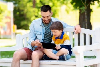family, fatherhood and technology concept - happy father and little son with tablet pc computer sitting on bench at summer park. father and son with tablet pc computer at park