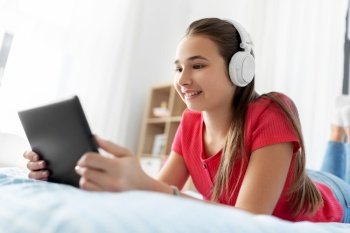 children, technology and communication concept - smiling teenage girl in headphones listening to music on tablet computer at home. girl in headphones listening to music on tablet pc