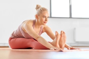 fitness, sport and healthy lifestyle concept - happy young woman doing yoga and seated forward bend at home. woman doing yoga and seated forward bend at home