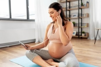 sport and people concept - happy smiling pregnant woman with earphones and smartphone doing yoga at home. pregnant woman with earphones doing yoga at home