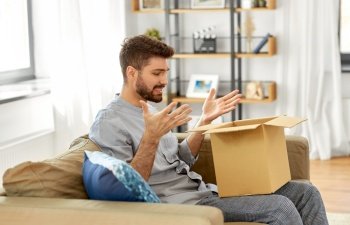 mail delivery, shipment and people concept - disappointed man opening parcel box at home. disappointed man opening parcel box at home