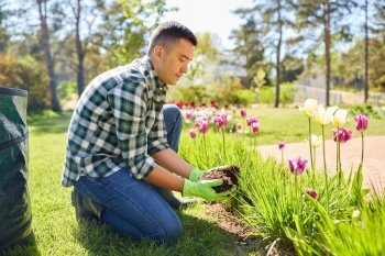 gardening and people concept - man pouring soil to flowers at summer garden. man pouring soil to flowers at summer garden