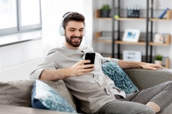 technology, leisure and people concept - happy man in headphones with smartphone listening to music at home. man in headphones listening to music on smartphone