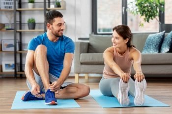 sport, fitness, lifestyle and people concept - smiling man tying laces and woman stretching at home. happy couple exercising at home