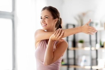 sport, fitness and healthy lifestyle concept - smiling young woman stretching arm at home. smiling young woman stretching arm at home