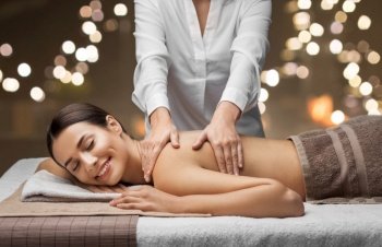 wellness, beauty and relaxation concept - beautiful young woman lying and having back massage at spa over festive lights on background. woman lying and having back massage at spa