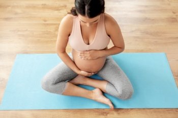 sport, fitness and people concept - happy pregnant woman sitting on yoga mat at home. happy pregnant woman sitting on yoga mat at home