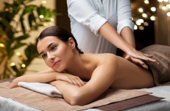 wellness, beauty and relaxation concept - beautiful young woman lying and having back massage at spa over festive lights on background. woman lying and having back massage at spa