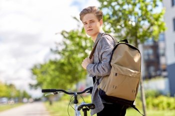 lifestyle, transport and people concept - young man or teenage boy with bicycle and backpack looking back on city street. young man with bicycle and backpack on city street