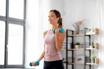 fitness, sport and healthy lifestyle concept - smiling young woman with dumbbells exercising at home. smiling young with dumbbells exercising at home