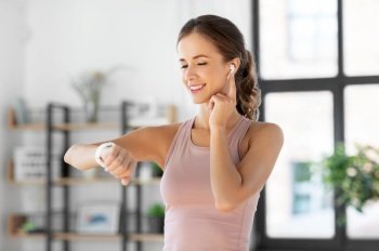sport, fitness and technology concept - happy smiling young woman with smart watch and earphones exercising at home. woman with smart watch and earphones doing sports