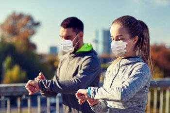 fitness, sport and health concept - couple wearing face protective medical mask for protection from virus disease with heart-rate watch doing sports over city highway bridge. couple in masks running over city highway bridge