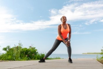 fitness, sport and healthy lifestyle concept - young african american woman exercising on beach. young african american woman exercising on beach