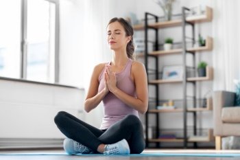 yoga, sport and healthy lifestyle concept - woman meditating in lotus pose at home. woman doing yoga in lotus pose at home