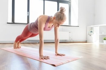 fitness, sport and yoga concept - young woman doing high plank exercise on mat at home. young woman doing plank exercise on mat at home
