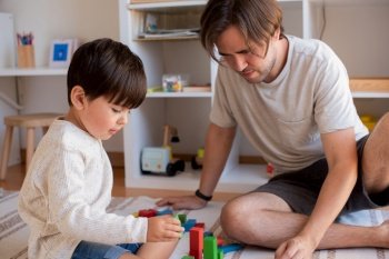 Little kid and his father playing at home with wood building blocks. Homeschooling. Stay at home. Family time