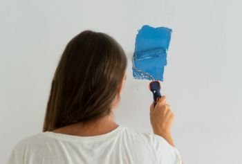 Woman painting wall of her house, do it yourself home renovation concept. Woman painting wall
