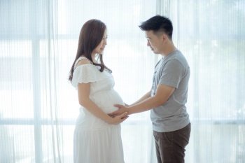 Young asian couple expecting baby standing together indoors