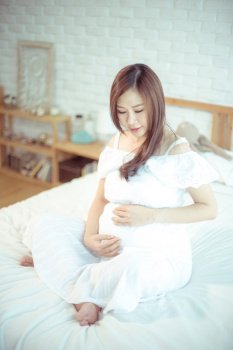 Attractive pregnant asian woman in bed and holding her belly
