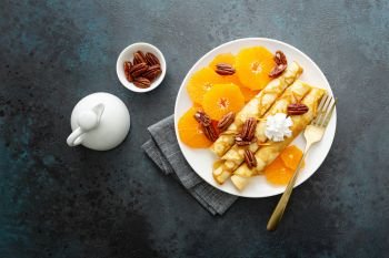 Crepes, thin pancakes with fresh tangerine slices, pecan nuts, syrup and whipped cream