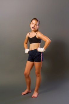 little girl in a sports tank top and shorts with hands wrapped in protective bandage is engaged in martial arts on a dark background. little mma girl