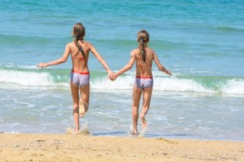 Girls holding hands run into the sea