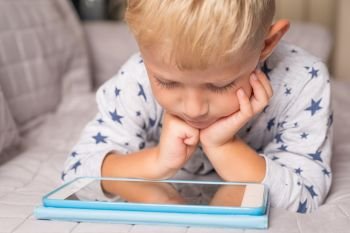 Caucasian child boy using digital tablet while lying on sofa at home