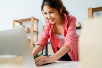 Young Asia entrepreneur businesswoman check product purchase order on stock and save to computer laptop work at home office. Small business owner, online market delivery, lifestyle freelance concept.