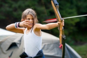 Happy girl shooting with a bow and arrow in a forest camp with gypsy children