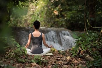 Young woman in yoga pose sitting near waterfall