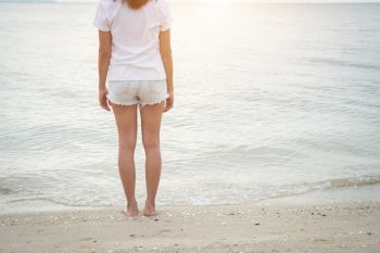Young woman standing on the beach with barefoot.