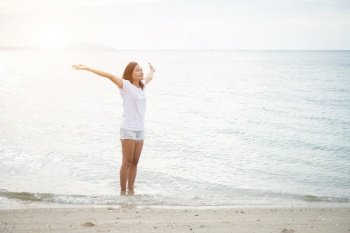 Young beautiful woman standing stretch her arms in the air on the beach with barefoot. Relaxing holiday. 