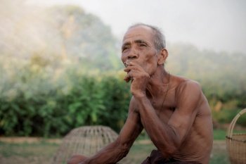 Old man are smoking in field of Thailand.