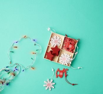 burning christmas garland on a white wire with colorful lights and box with wooden toys for the Christmas tree on a green background