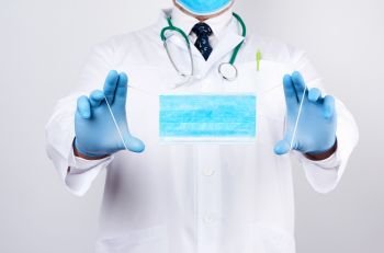 doctor in a white coat, blue latex sterile gloves holds textile medical masks in his hand on a white background, protective accessory against viruses and bacteria