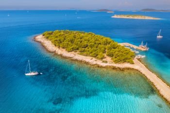 Aerial view of beutiful small island in sea bay at sunny day in summer in Murter, Croatia. Top view of transparent blue water, green trees, mountain, sandy beach, boats and yachts. Tropical landscape