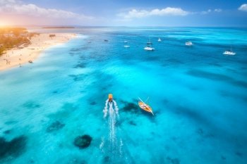 Aerial view of the yachts, fishing boats on tropical sea coast with sandy beach at sunset. Summer travel in Zanzibar, Africa. Landscape with boats in clear blue water, green palm trees. Top view. Aerial view of the fishing boats on the tropical sea coast