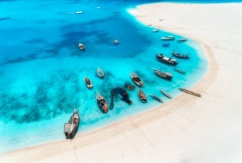 Aerial view of the fishing boats and yachts on tropical sea coast with white sandy beach at sunset in summer. Zanzibar, Africa. Colorful landscape with boats, transparent blue water. Top view. Travel. Aerial view of the fishing boats and yachts on tropical sea coast