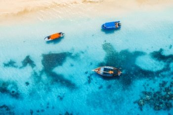 Aerial view of the fishing boats in clear blue water at sunny day in summer. Top view from drone of boat, yacht, sandy beach in Zanzibar. Travel. Tropical seascape with sailboats, sea. View from above