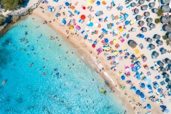 Aerial view of sandy beach with colorful umbrellas, swimming people in sea bay with transparent blue water at sunset in summer. Travel in Mallorca, Balearic islands, Spain. View from above. Landscape