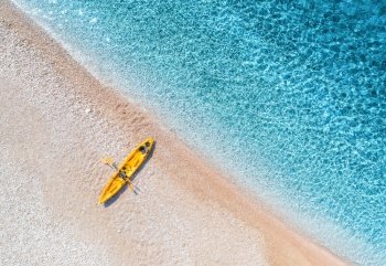 Aerial view of empty sandy beach with yellow canoe, sea coast with transparent blue water in sunny bright day in summer. Travel in Croatia. Top view of boat. Landscape with kayak at sunset. Travel