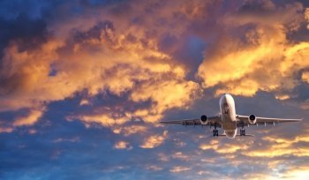 Airplane is flying in colorful sky at sunset. Landscape with white passenger airplane, purple sky with pink clouds. Aircraft takes off. Business trip. Commercial plane. Travel. Aerial view. Concept
