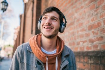 Portrait of young handsome man listening to music with headphones against brick wall. Urban concept.