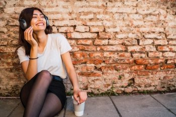 Portrait of young latin woman relax and listening to music with headphones against brick wall. Urban concept.